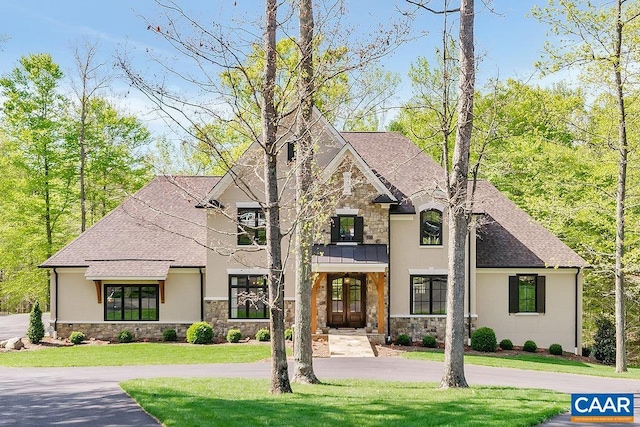 french country home featuring stone siding, stucco siding, roof with shingles, and a front yard