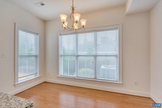 unfurnished dining area with baseboards, a chandelier, visible vents, and light wood-style flooring