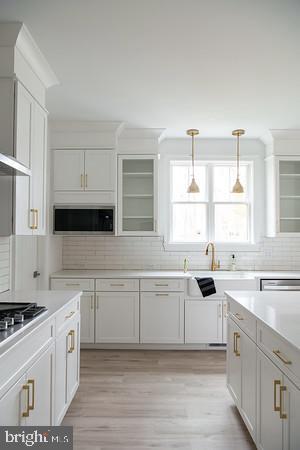 kitchen with stainless steel microwave, decorative light fixtures, decorative backsplash, stovetop, and white cabinets