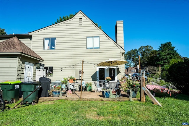 rear view of property featuring a yard, a patio area, and a chimney