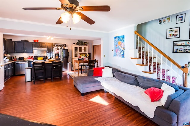 living area with crown molding, wood finished floors, ceiling fan, and stairs