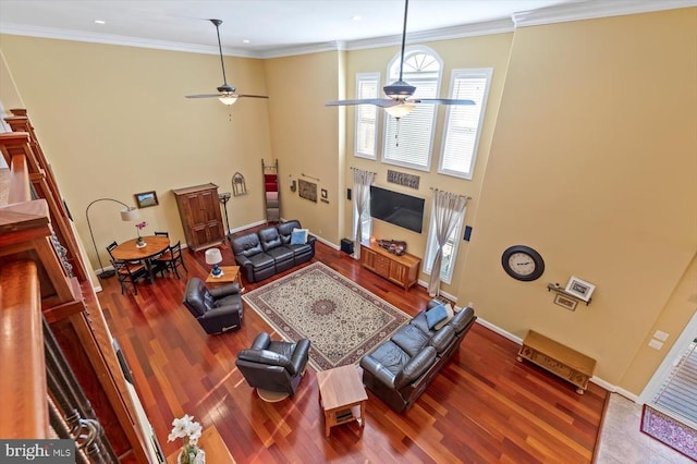living area featuring ceiling fan, wood finished floors, a towering ceiling, baseboards, and crown molding