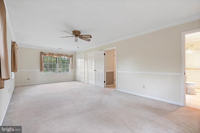  - unfurnished bedroom with carpet flooring, ornamental molding, ensuite bath, multiple closets, and ceiling fan