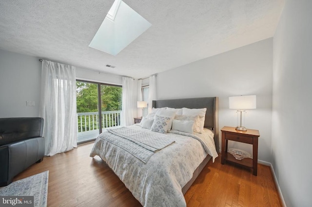  - bedroom with access to outside, wood finished floors, a textured ceiling, a skylight, and baseboards