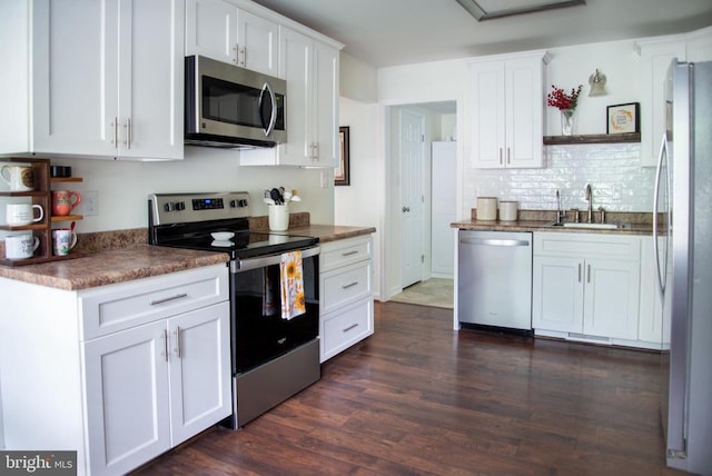 kitchen with appliances with stainless steel finishes, a sink, dark wood finished floors, and white cabinetry