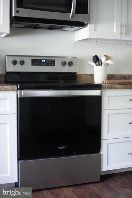 kitchen view of appliances with stainless steel finishes, white cabinets, and dark wood-style flooring