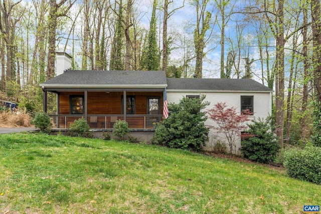 view of front of home with covered porch, a chimney, and a front yard