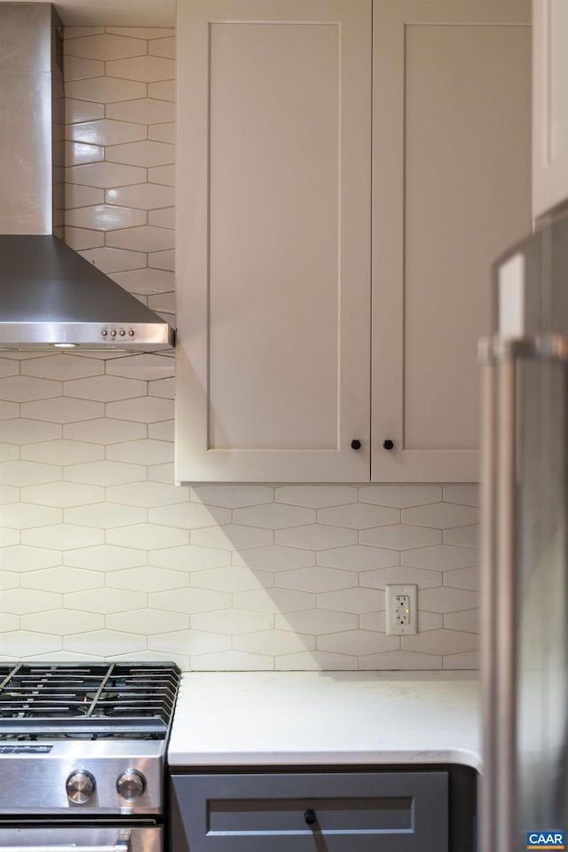 kitchen with stainless steel gas range oven, backsplash, light countertops, and wall chimney exhaust hood