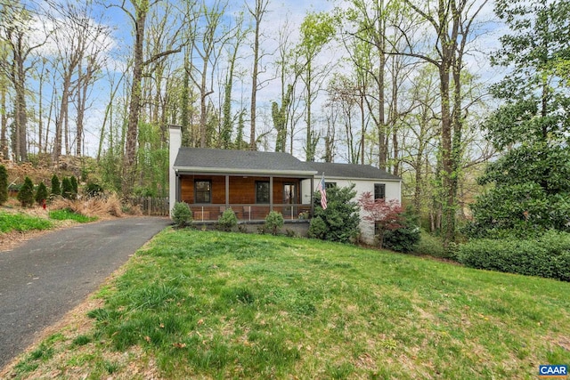 view of front of property with covered porch, driveway, a chimney, and a front lawn
