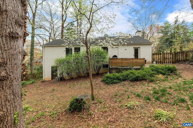 back of house with brick siding, a chimney, fence, and a deck