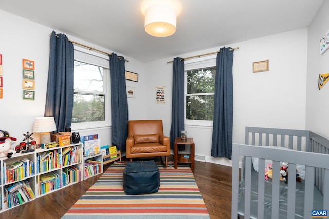 bedroom with a nursery area, multiple windows, dark wood finished floors, and visible vents