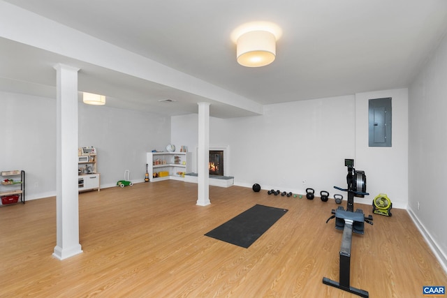 workout area featuring electric panel, wood finished floors, a lit fireplace, and baseboards