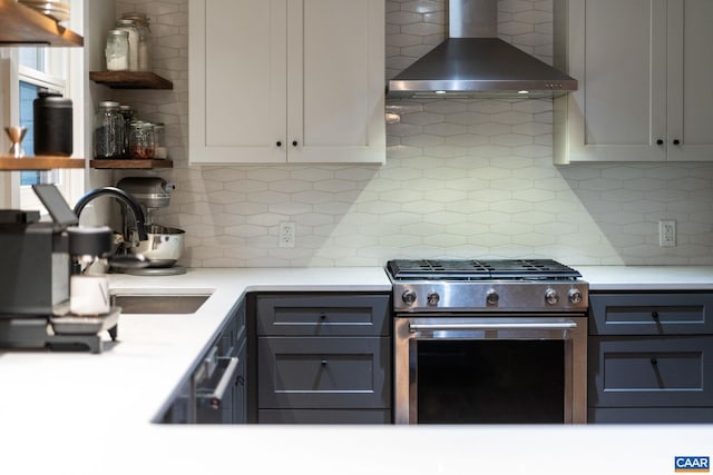 kitchen featuring stainless steel range with gas stovetop, decorative backsplash, light countertops, and wall chimney exhaust hood