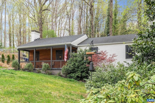 view of front of house featuring a porch, a shingled roof, a chimney, and a front yard