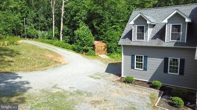 view of home's exterior with driveway, a shingled roof, a storage shed, and an outdoor structure