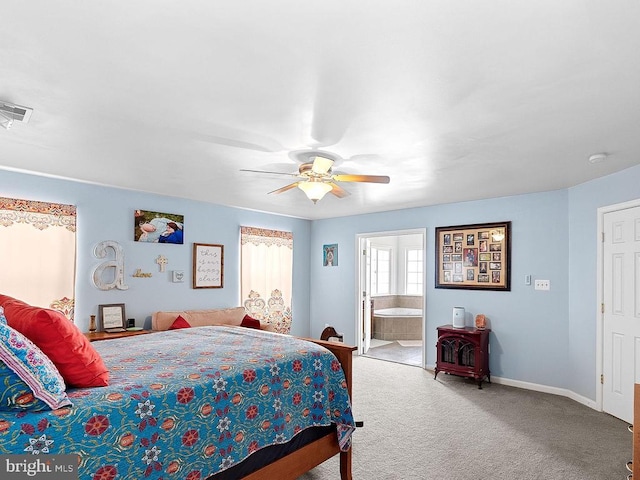  - carpeted bedroom featuring ceiling fan, baseboards, ensuite bathroom, and a wood stove