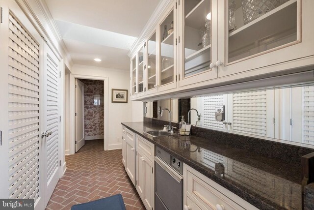  - kitchen featuring brick floors, dark stone counters, crown molding, glass insert cabinets, and white cabinetry