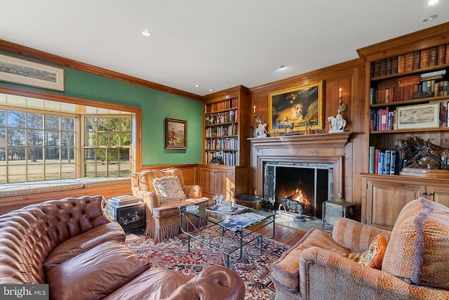  - living area with built in features, wainscoting, crown molding, recessed lighting, and a fireplace with flush hearth