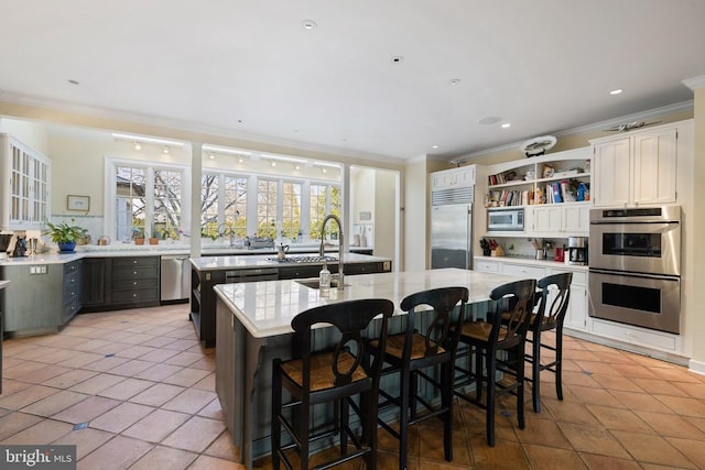  - kitchen with built in appliances, a center island with sink, crown molding, open shelves, and light tile patterned flooring