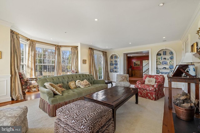  - living room featuring built in shelves, stairs, wood finished floors, crown molding, and a wainscoted wall