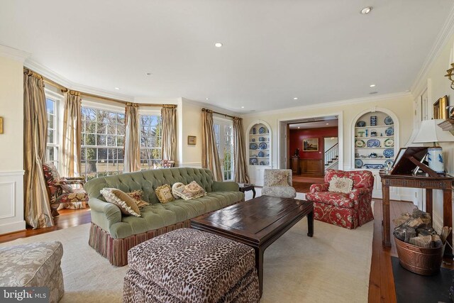  - living area featuring built in shelves, stairway, wood finished floors, crown molding, and wainscoting