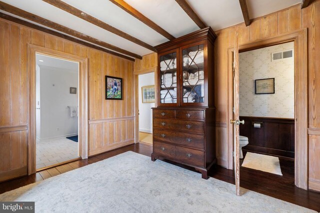  - bedroom with beamed ceiling, wood finished floors, wood walls, ensuite bath, and a wainscoted wall