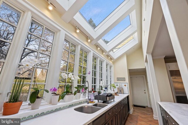  - kitchen with a skylight, dark brown cabinets, light tile patterned floors, rail lighting, and a towering ceiling