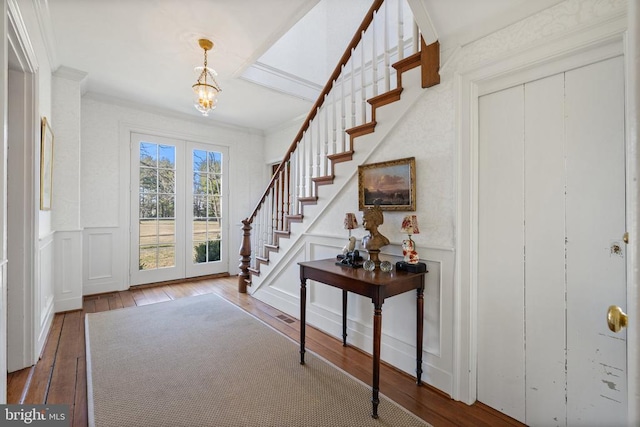  - foyer entrance with hardwood / wood-style floors, stairway, a decorative wall, wainscoting, and a chandelier