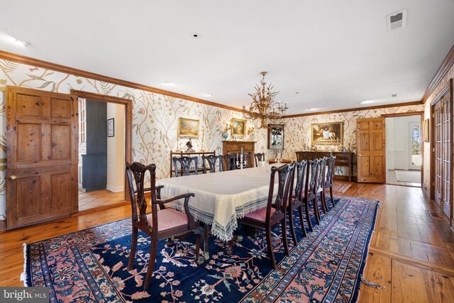  - dining space featuring wallpapered walls, ornamental molding, hardwood / wood-style flooring, and a chandelier