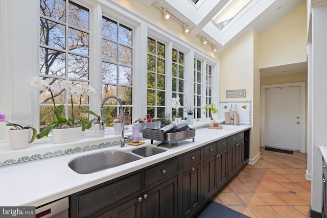  - kitchen featuring rail lighting, a skylight, light countertops, light tile patterned flooring, and lofted ceiling