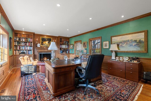  - office with wood finished floors, recessed lighting, built in features, a lit fireplace, and crown molding