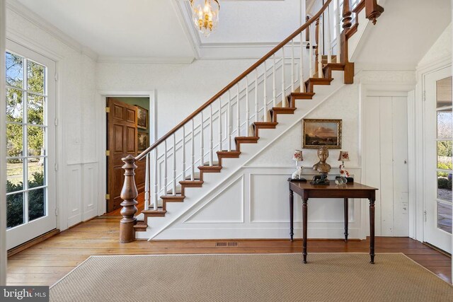  - foyer featuring a decorative wall, wood-type flooring, stairway, a chandelier, and crown molding