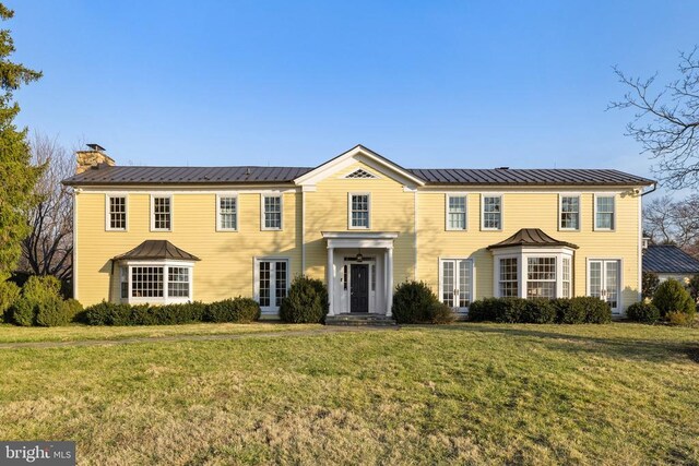  - colonial-style house with a chimney, a front yard, and a metal roof
