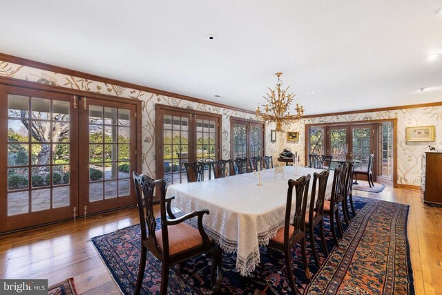  - dining room featuring french doors, wallpapered walls, ornamental molding, wood-type flooring, and a chandelier