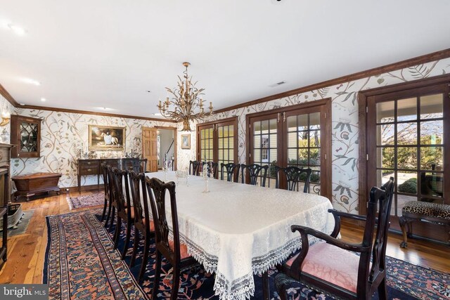  - dining space featuring wallpapered walls, french doors, crown molding, hardwood / wood-style floors, and a chandelier
