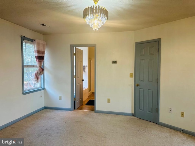carpeted spare room with a chandelier, visible vents, and baseboards