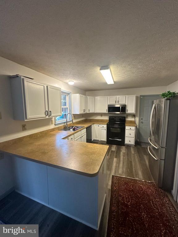 kitchen with white cabinets, a peninsula, dark wood-style floors, a sink, and black appliances