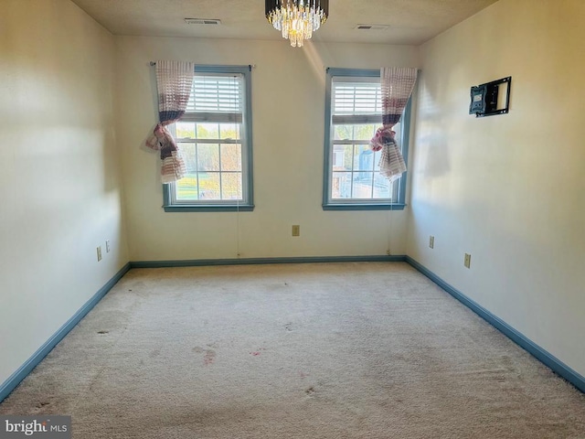 unfurnished room with carpet, visible vents, baseboards, and a notable chandelier