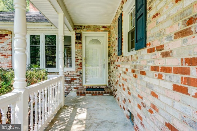  - view of exterior entry featuring covered porch, brick siding, and roof with shingles