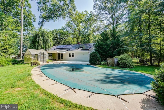  - view of swimming pool with a greenhouse, a covered pool, a lawn, a patio area, and an outbuilding