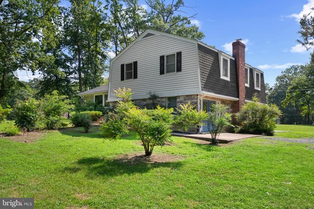  - view of property exterior featuring a gambrel roof, a chimney, a yard, stone siding, and roof with shingles