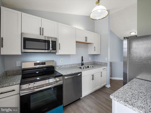 kitchen featuring stainless steel appliances, a sink, vaulted ceiling, white cabinetry, and light wood-type flooring