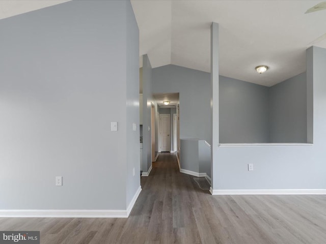 hallway featuring vaulted ceiling, wood finished floors, and baseboards