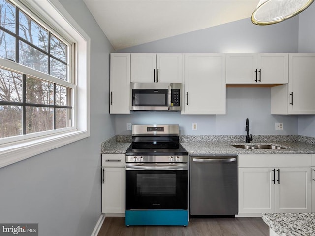kitchen with vaulted ceiling, a sink, white cabinetry, wood finished floors, and stainless steel appliances