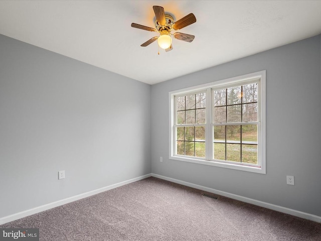 carpeted empty room with baseboards, visible vents, and a ceiling fan