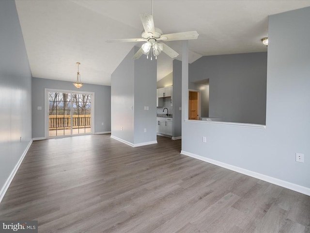 unfurnished living room featuring a sink, wood finished floors, vaulted ceiling, ceiling fan, and baseboards
