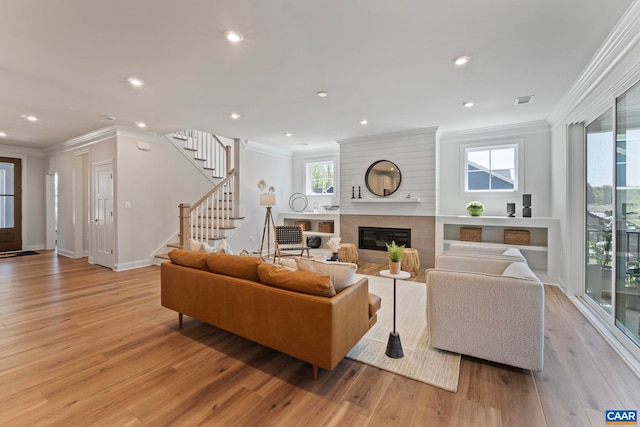 living room with light wood-style floors, stairway, ornamental molding, and a glass covered fireplace