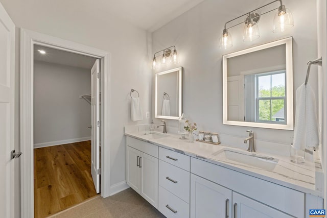 full bath with baseboards, double vanity, a sink, and a walk in closet