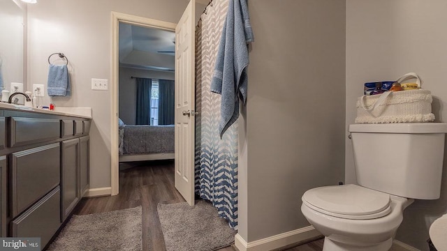ensuite bathroom with toilet, wood finished floors, baseboards, ensuite bath, and vanity