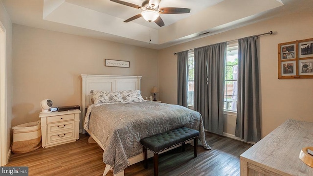 bedroom with ceiling fan, a tray ceiling, visible vents, and wood finished floors